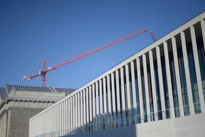 Low angle view of crane by building against clear blue sky