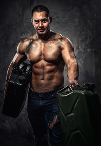 Portrait of shirtless muscular worker holding cans while standing against wall