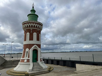 Lighthouse amidst sea and buildings against sky