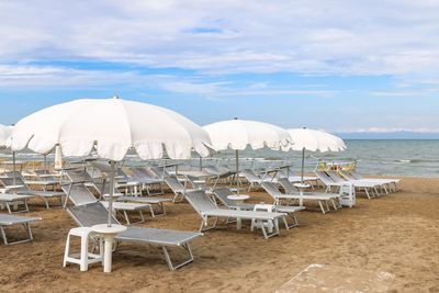 Deck chairs on beach against sky