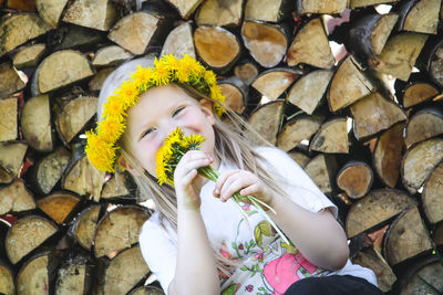 A little girl with a wreath on her head sitting near the firewood stack outdoors.