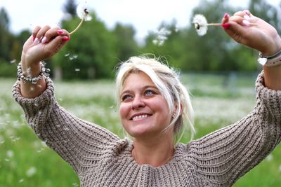 Smiling woman holding dandelion outdoors