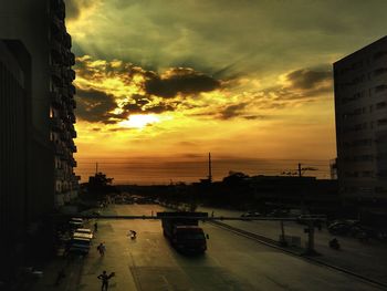 Cars on city street against sky during sunset