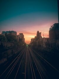 Railroad tracks amidst buildings against sky during sunset