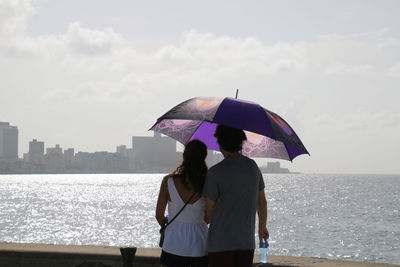 Rear view of couple with umbrella looking at city and sea