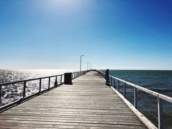 Pier over sea against clear blue sky