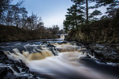 Scenic view of waterfall in forest against clear sky