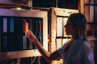 Side view of woman holding card while standing by board