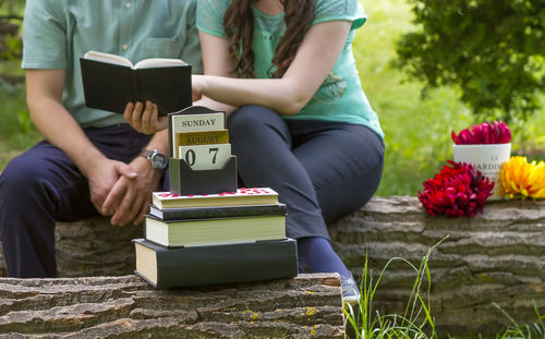 Midsection of woman holding book while sitting by potted plant