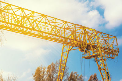 Yellow gantry crane behind the trees on the territory of the enterprise. industry, warehouse