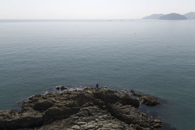 Distant view of person fishing while standing at beach against clear sky during sunny day