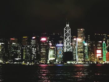 Illuminated buildings by river against sky at night