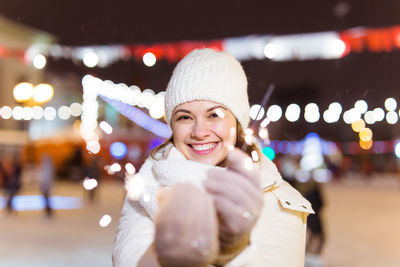 Portrait of smiling young woman in illuminated park during winter