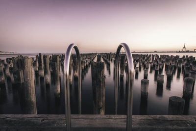 View of wooden posts in sea during sunset