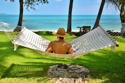 Rear view of shirtless man sitting on shore