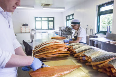 Worker cutting fish while senior worker working at counter in food processing plant