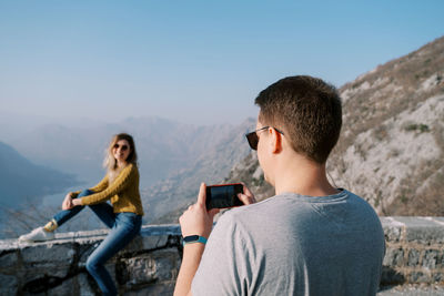 Side view of young man photographing against mountain