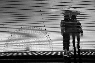 Reflection of friends with umbrella and ferris wheel on wet walkway