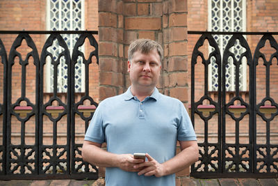 Portrait of man standing by gate against building