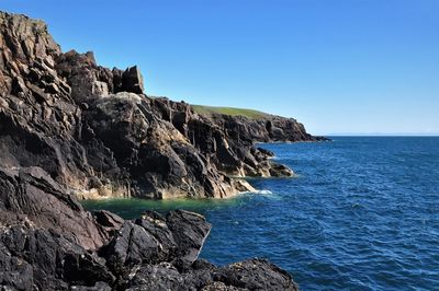 Scenic view of rock formation in sea against clear blue sky