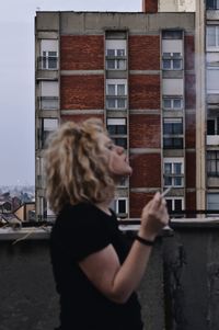 Portrait of woman holding umbrella against building in city