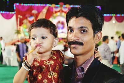 Portrait of father carrying daughter at party during night