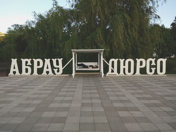 Information sign on tiled floor against trees in city