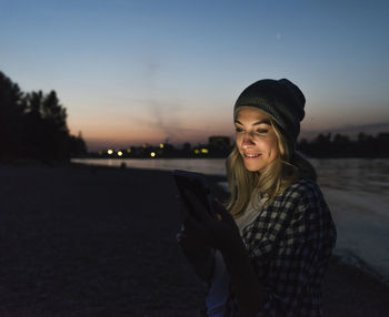 Young woman using smartphone on riverside in the evening
