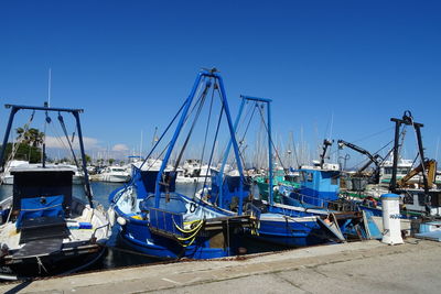 Boats moored at harbor against clear blue sky