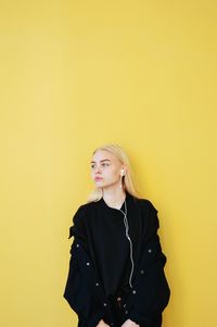 Beautiful young woman standing against yellow wall