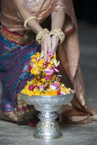 Low section of woman picking flower petals from silver container at temple