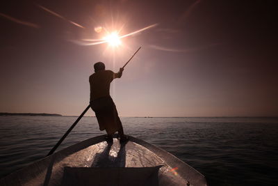 Man rowing boat in river against sky on sunny day