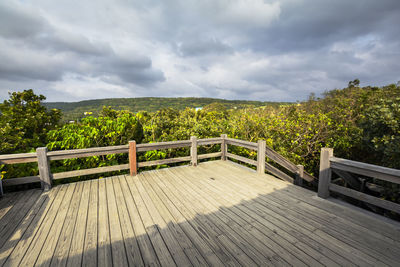 View of wooden footbridge against trees and sky