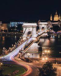 Illuminated bridge over river in city at night