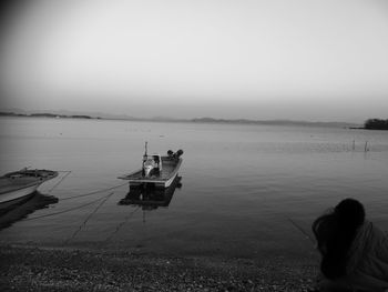 Rear view of men on boat moored in sea against clear sky