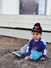 Cute boy sitting on ground outdoors