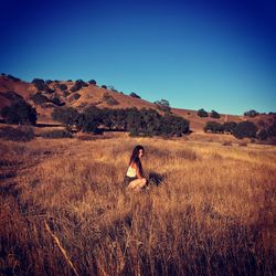 Woman crouching at grassy field against clear blue sky