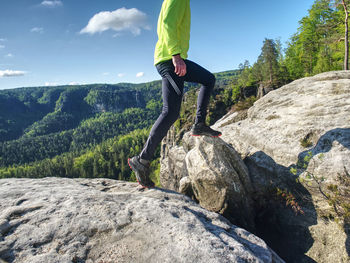 Fitness man trail runner running to rocky mountain top on cracked rocky block.