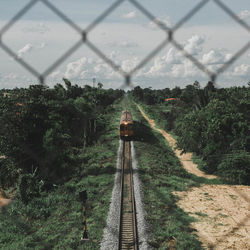 High angle view of train moving amidst trees against sky seen through fence