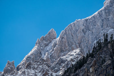 Low angle view of snowcapped mountains against clear blue sky