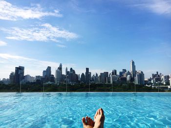 Low angle view of person floating on swimming pool against city