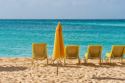 Deck chairs on beach by sea against sky