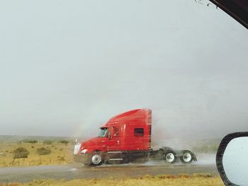 Cars on wet road by sea against sky