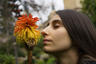 Young woman smelling a flower called kniphofia in a garden.