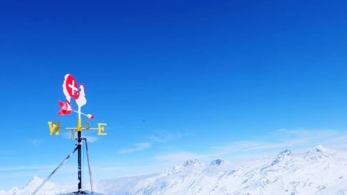 Low angle view of sign on snow covered mountain against blue sky