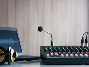 Close-up of sound mixer and microphone on table against wooden wall