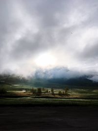 Road passing through field against cloudy sky