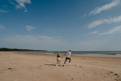 Rear view of woman walking at beach against sky