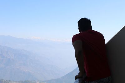 Rear view of man looking at mountains against sky