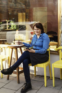 Happy owner using digital tablet while sitting at sidewalk cafe